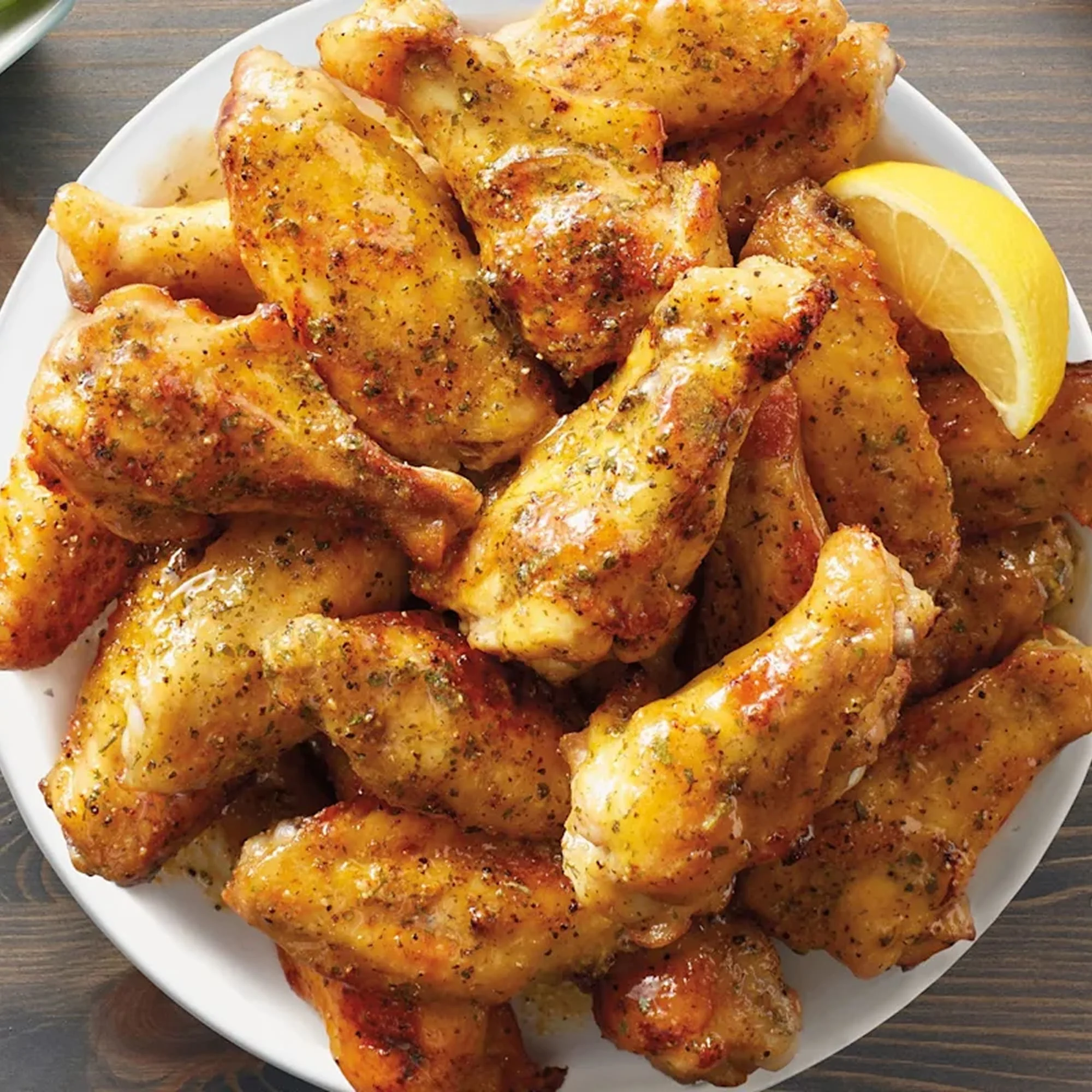 A plate of lemon pepper wings with a lemon wedge